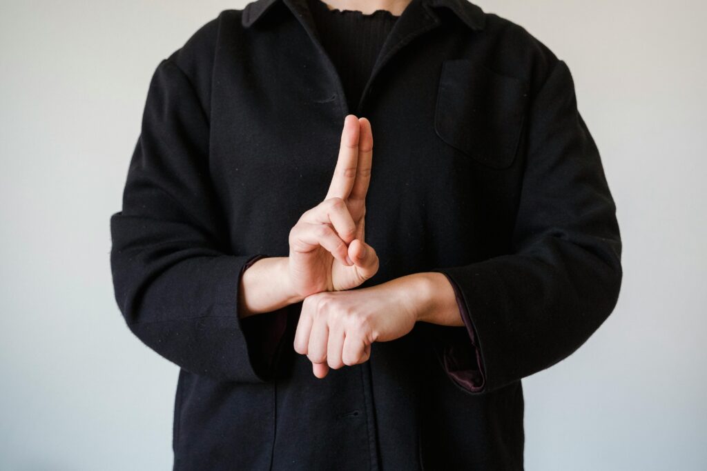 A person in a black coat demonstrating a sign language gesture indoors.